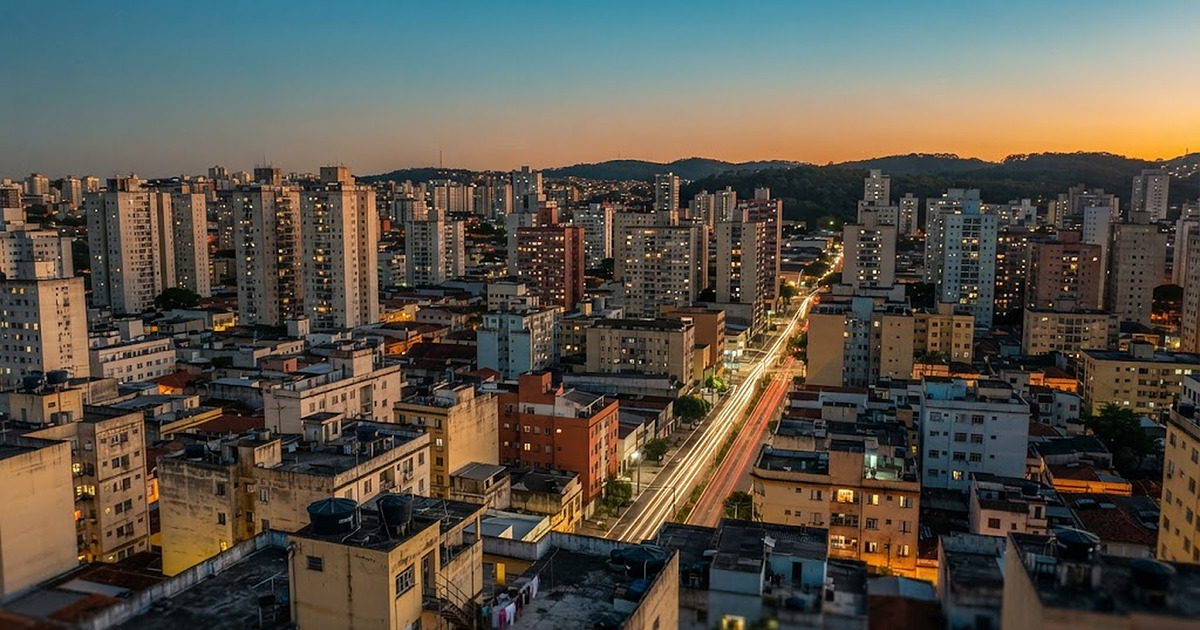 The center of Guarulhos seen from above at dusk, with residential towers, a lit avenue and wooded hills behind